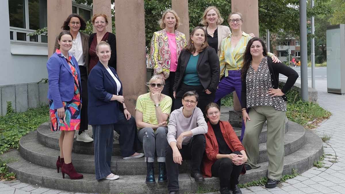 Gruppe von Frauen stehen und sitzen auf Stufen zwischen Betonpfeilern